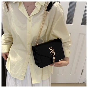 Detail of black crossbody bag with gold S-logo, elegant fringe, and metal chain strap