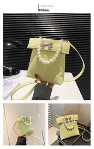 Detail of yellow crossbody bag featuring metal bow decoration and elegant pearl handle