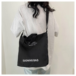 Close-up of black canvas tote bag with adjustable strap worn by a model in a studio