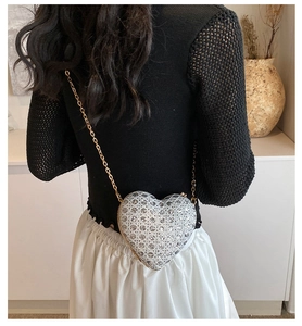 Silver sequin heart bag with gold chain strap worn by a model in a stylish home setting