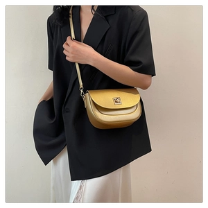Sac selle doré chic porté avec un blazer noir et une jupe en dentelle blanche