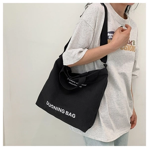 Detail of a black canvas tote bag with white lettering worn by a model in a natural setting