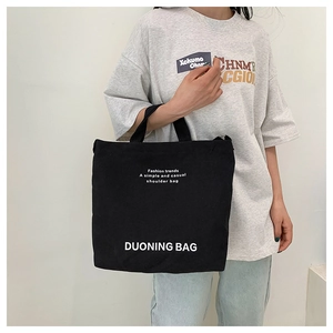 Detailed view of black canvas tote bag with white fashion slogan and wide shoulder straps