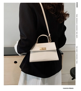 Model wearing a minimalist cream crossbody bag with top handle and gold hardware detail