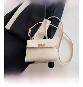 Cream-colored mini crossbody bag with gold buckle next to a smartphone for size reference