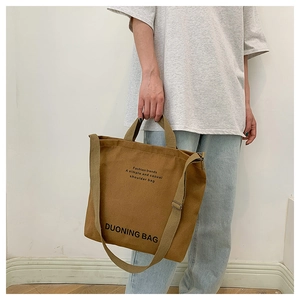 Brown canvas tote bag detail showing dual handles and wide shoulder strap on model