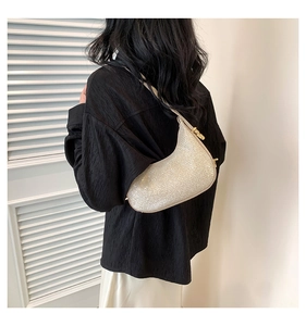 Silver sequin crescent underarm bag with gold buckle shown on shoulder of a model