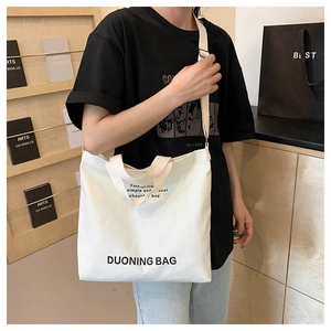 Detail of white canvas tote bag with black DUONING text and adjustable shoulder strap
