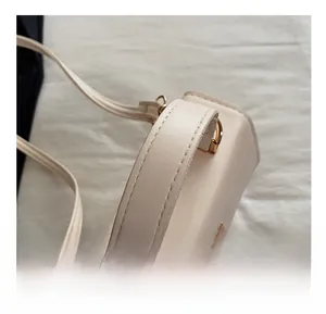 Detail of soft leather handle with premium gold metal rings on a white crossbody bag