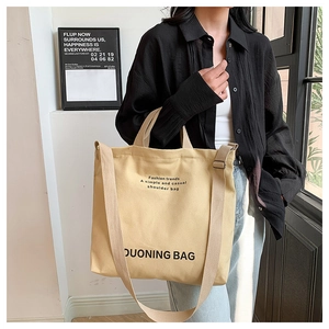 Detail of beige canvas tote bag with black text print showing the dual handle design