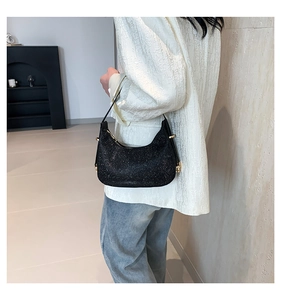 Close-up of black glitter shoulder bag with gold hardware worn by a model