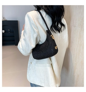 Detail of a sparkling black sequin baguette bag with gold metal hardware worn on shoulder