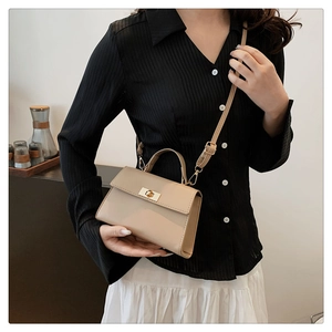 Detail view of stylish beige square handbag with golden twist lock on a shoulder strap