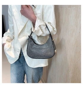 Close-up of a sparkling silver rhinestone crescent shoulder bag worn with a white blazer