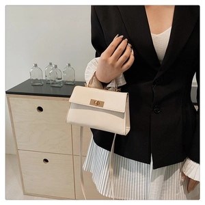 Close-up of the cream trapezoid handbag featuring gold twist lock and smooth texture