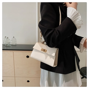 Detail of a creamy white crossbody bag with a gold twist lock on a minimalist outfit