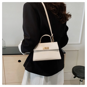 Minimalist beige trapeze handbag with gold clasp worn as a crossbody by a model