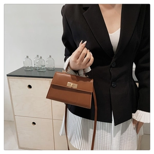 Detail of a brown leather trapezoid handbag with a metal twist-lock and detachable strap