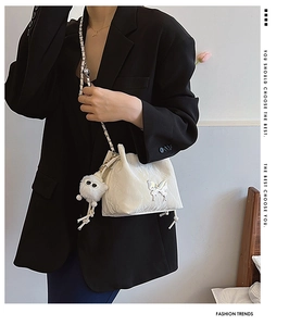 Detail of white textured bucket bag featuring silver butterfly clasp and plush charm