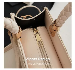Detail view of golden zipper closure and braided handle on cream woven tote bag