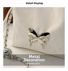 Detail of silver metal butterfly charm and woven chain on a white pleated bucket bag