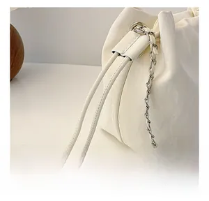 Detailed close-up of textured white bucket bag with drawstring and silver chain strap