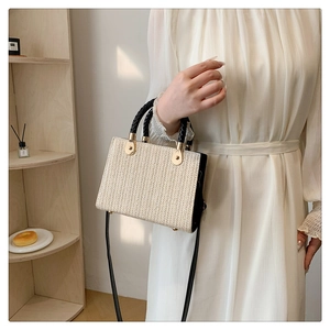 Detail of woven straw tote bag with black leather accents and golden hardware detail