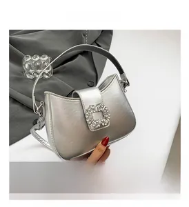 Detail of silver crossbody bag with sparkling rhinestone buckle on a textured fabric surface
