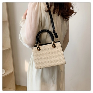 Detail of beige woven square bag with herringbone pattern and black ring handle