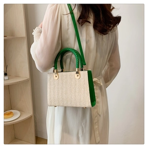 Detail of a straw tote bag with green handles and gold metal clasp on a model shoulder