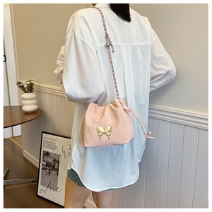 Detail of pink bucket bag featuring golden butterfly buckle and woven chain strap
