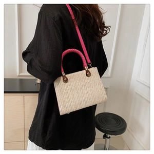 Detail of woven straw handbag with pink braided handle and metallic feet on a model