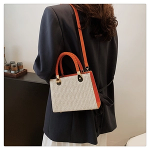 Detail of woven straw handbag featuring orange leather trim and round braided handle