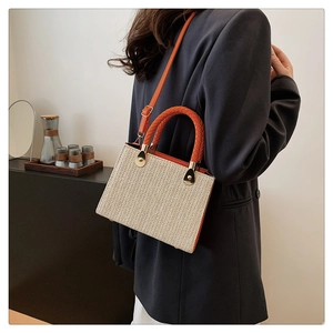 Close-up of woven straw tote featuring orange braided handles and gold ring accents