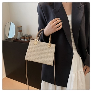 Detail of beige straw tote bag with brown woven handles and metallic hardware accents
