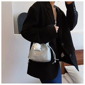 Silver metallic drawstring bucket bag with butterfly pendant and fluffy pompom detail
