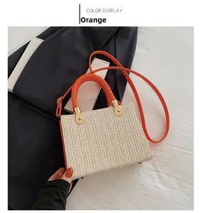 Detail of woven straw handbag featuring orange braided handles and gold-tone hardware