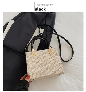 Detailed view of woven straw handbag with black cylindrical handles and gold hardware