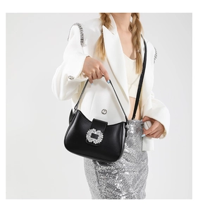 Detail of a black crescent PU shoulder bag with sparkling crystal buckle on white blazer