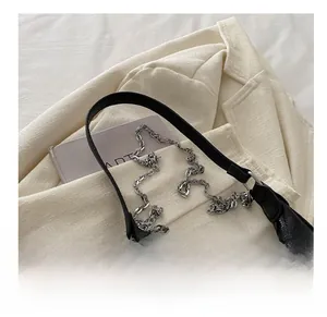 Detail of black pebbled leather hobo bag with chunky silver chain on tweed jacket
