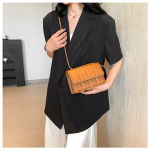 Brown quilted crossbody bag with gold chain strap worn by a model in a black blazer