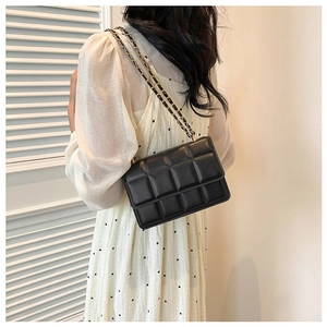 Elegant black quilted chain shoulder bag worn by model in stylish polka dot dress