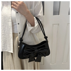 Detail of black patent leather shoulder bag with a large decorative bow and slim straps