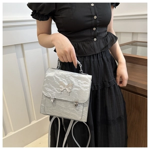 Silver grey bow-accented backpack with pleated texture and dual metal buckles on model