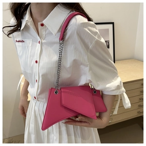 Close-up of fuchsia geometric asymmetrical bag with silver chain on white outfit