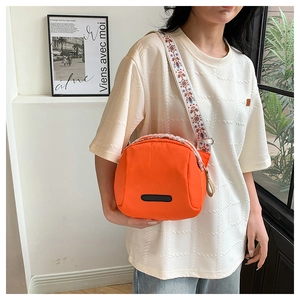 Detail of a bright orange nylon crossbody bag with vintage embroidered wide shoulder strap