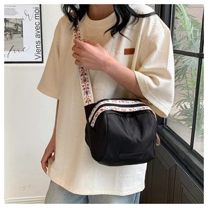 Detail of a black nylon shell bag featuring a colorful ethnic style embroidery strap