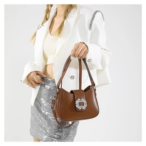 Brown crescent shoulder bag with rhinestone buckle shown on a model with a white suit