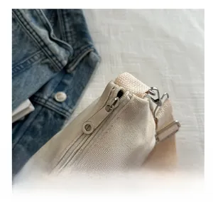 Close-up of smooth metal zipper and canvas texture on a minimalist cream shoulder bag