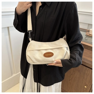 Close-up of cream canvas crossbody bag with brown leather logo patch and strap details